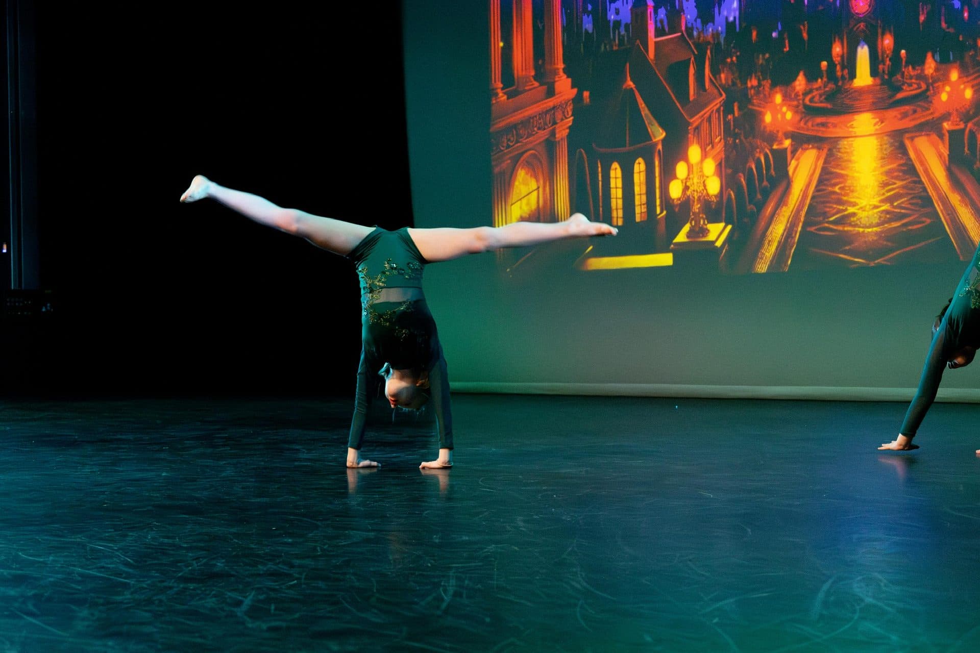 An acro student in a handstand split on stage