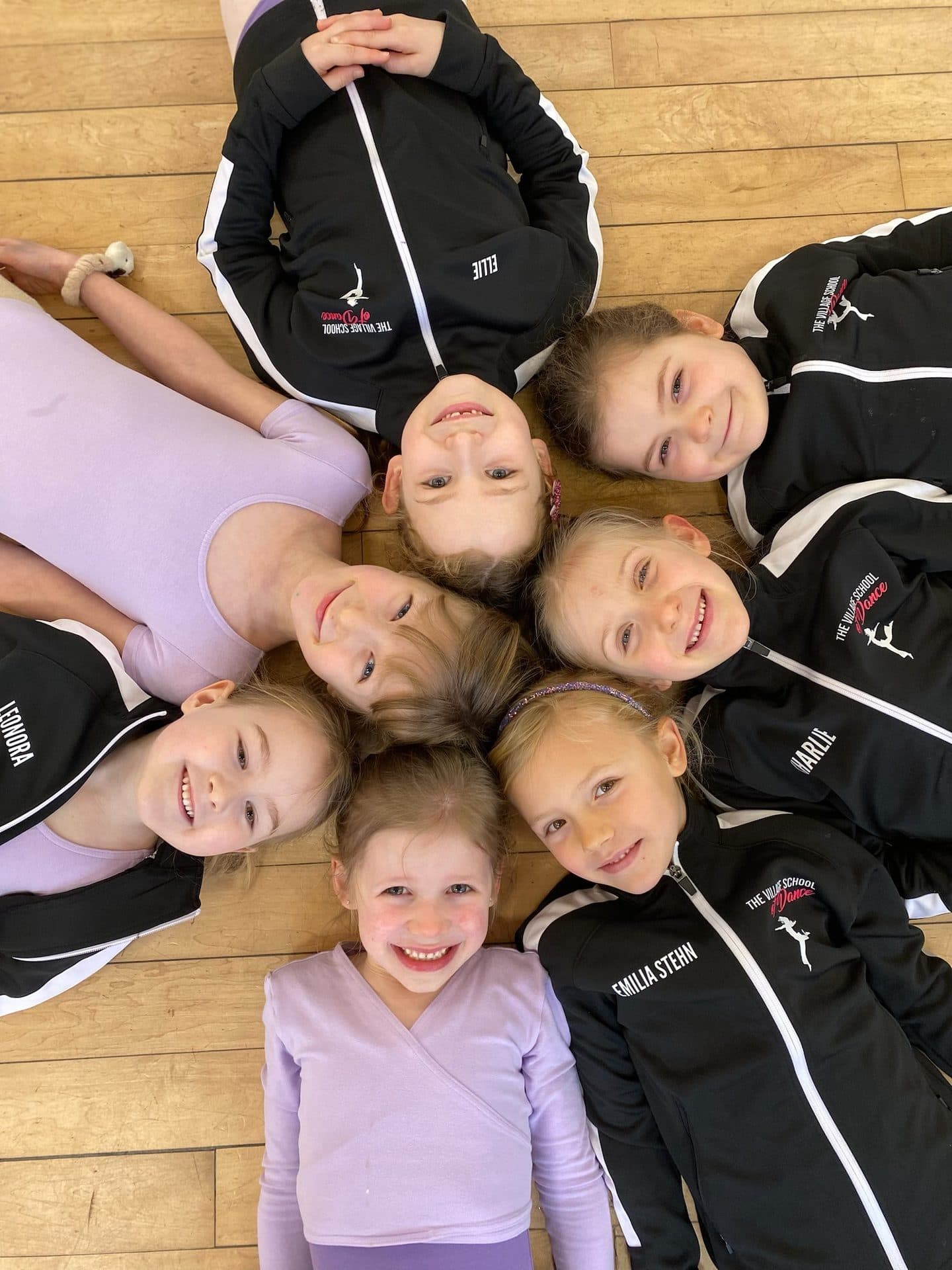 Young dancers looking up and smiling from a circle on the studio floor